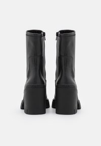 Paire de bottes mi-mollet en cuir noir avec talons hauts épais, fermetures éclair à l'arrière et nom de la marque embossé au-dessus du talon.