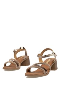 Sandalias de tacón de bronce con correas entrelazadas, una correa de tobillo texturizada con hebilla y una plantilla de color marrón claro. Tacón cuadrado.