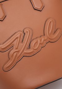 Gros plan d'un sac en cuir marron avec le mot en cursive "You" cousu en patch décoratif en relief.