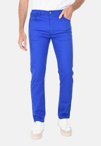 Chinos blu brillanti con un design aderente, dotati di zip, tasche frontali e una texture liscia. Abbinati a sneaker chiare.