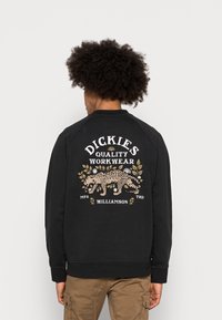 Svart sweatshirt med en grafisk design som föreställer en leopard, blommönster och texten "DICKIES QUALITY WORKWEAR" på baksidan. Blandat bomullstyg.