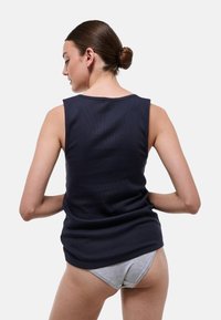 Débardeur bleu marine côtelé avec larges épaules, col rond et coupe décontractée, vu de dos. Un sous-vêtement gris est également visible.