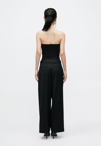 Haut noir sans bretelles associé à un pantalon noir à jambes larges. Le haut présente une coupe ajustée, tandis que le pantalon a une finition sur mesure avec des poches.