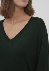 Mørkegrøn strikket sweater med V-hals, ribbet kant og løstsiddende ærmer. Blød tekstur og lette udseende.