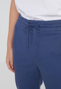 Námořnické modré kalhoty vyrobené z lehkého materiálu, s elastickým pasem a tkaničkou, a bočními kapsami. Hladká textura a jednoduchý design.