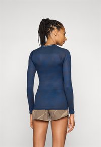 Langermet atletisk topp i marine med teksturert design, med en tettsittende fasong og rund hals, kombinert med mønstrede shorts.