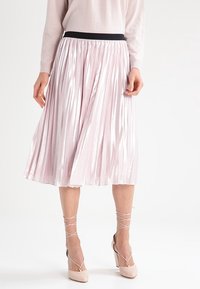 Rosa plisserad midikjol med svart elastisk midjeband, med en glänsande textur och mjukt fall, kombinerad med ljusa högklackade skor.