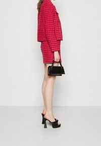 Completo giacca e gonna con motivo houndstooth rosa dal design cropped. Borsa nera con una forma strutturata e texture liscia. Sandali con tacco alto.
