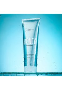 Tube de revitalisant brillant étiqueté "Color Wow Money Laundering" avec des gouttes d'eau sur fond bleu.