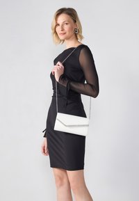 Λευκή τσάντα clutch με σχέδιο φακέλου, ασημένια αλυσίδα και καπάκι με στρασάκια. Ματ φινίρισμα; κομψή και ορθογώνια σιλουέτα.