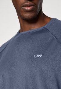 Ναυτικό μπλε αθλητικό μπλουζάκι από ύφασμα που απωθεί την υγρασία, με στρογγυλή λαιμόκοψη και λευκό λογότυπο "ICIW" στο στήθος.