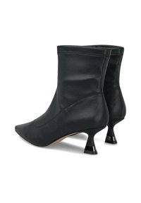 Botas de cuero negro hasta el tobillo con punteras afiladas y tacones cortos acampanados, exhibidas sobre un fondo blanco.