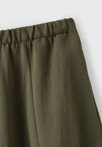 Tissu vert olive avec ceinture élastique, montrant un gros plan des coutures froncées et de la texture douce.