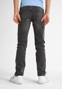 Jeans ajustados de color gris oscuro con dos bolsillos traseros, un sutil desvanecimiento y una pierna ligeramente tapered. Combinados con zapatillas blancas.