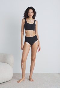 Black sports bra and high-waisted underwear set; smooth fabric, minimalist design, features light skin tone with contrasting lighter patches.