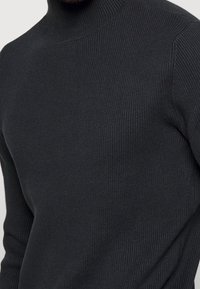 Svart ribbad polotröja, tillverkad av stickat material med en kroppsnära design och texturerad yta, som betonar värme och komfort.