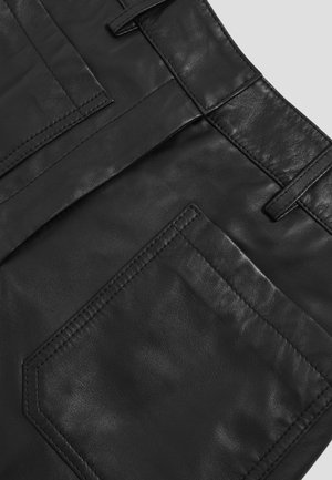 Juodų odinių kelnių detalė, rodanti galinį kišenę, diržo kilpas ir tekstūruotą siūlę ant lygaus odos audinio.