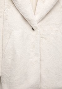 Fehér műszőrme kabát, bemetszett gallérral, nagy elülső zsebekkel, egy gombos záródással és puha, textúrált anyaggal.