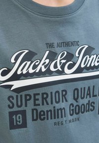 Siva pamučna majica s okruglim izrezom i odvažnim crno-bijelim grafičkim otiskom koji glasi "Jack & Jones Superior Quality Denim Goods."