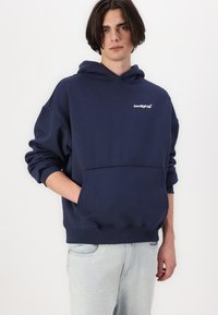 Felpa oversize blu navy in cotone, con tasca a marsupio, polsini a coste e un piccolo logo bianco sul petto.
