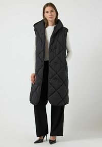 Svart, vadderad ärmlös rock med hög krage och knappstängning, med en slät textur och en lång, rak silhuett.