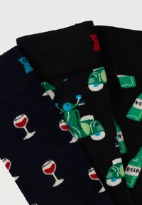 Τρία ζευγάρια διπλωμένων κάλτσες με σχέδια: ποτήρια κόκκινου κρασιού σε σκούρο μπλε, πράσινα σκούτερ σε μαύρο και πράσινα μπουκάλια μπύρας σε μαύρο.