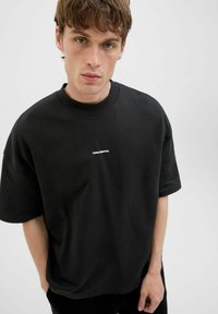 Schwarzes Baumwoll-T-Shirt mit Rundhalsausschnitt und kurzen Ärmeln. Zentrale weiße Schrift mit "CORE CREATIVE." Glatte Textur, lockere Passform.