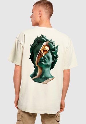 Cream-colored t-shirt featuring a graphic of a green and gold split bust design with decorative leaves, creating a contrasting texture.