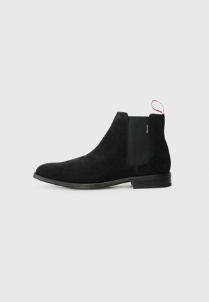 Bottines Chelsea en daim noir avec panneaux latéraux élastiques, bout arrondi et semelle en caoutchouc robuste. Comprend une bride pour un enfilage facile.