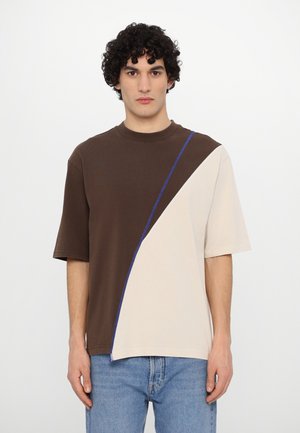 T-shirt color block marrone e crema con maniche corte, scollatura rotonda e un accento blu cucito diagonalmente attraverso il design.
