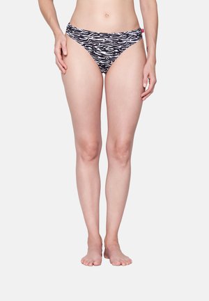 Woman wearing black and white zebra print bikini bottoms standing barefoot against a plain background.