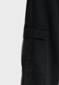 Zwarte cargobroek met een gladde textuur, voorzien van een zijzak, dubbele stiksels en een tapered fit. De stof lijkt duurzaam en veelzijdig.