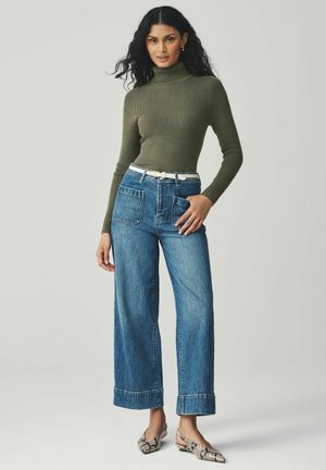 Olivově zelený proužkovaný rolák v kombinaci s volnými modrými džíny a krémovým páskem. Celý outfit doplňují baleríny s hadím potiskem.