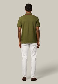 Olivovo zelená polo košeľa s krátkymi rukávmi, jednoduchý dizajn a červené akcenty, spojená s bielymi úzkymi džínsami a hnedými topánkami.