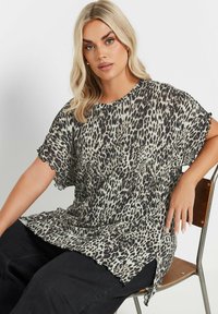 Top de estampado de leopardo en tejido ligero, con mangas cortas, escote redondo y dobladillo deshilachado. Combinado con pantalones oscuros.