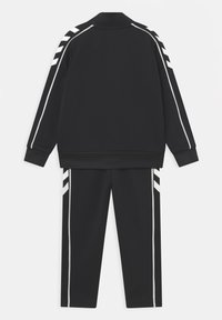 Chándal negro con chaqueta de cremallera y pantalones. Presenta acentos de franjas blancas en las mangas y los lados. Tejido atlético suave, corte estándar.