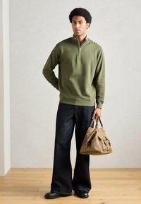 Roheline tõmblukuga pusa, tumedad laiad teksapüksid ja beež nahast käekott. Sujuv kangas, vabaaja stiil, peened riistvara detailid kotil.