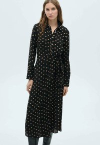 Robe noire à manches longues avec un devant à boutons, taille ceinturée et motif de points bruns éparpillés. Tissu lisse et coupe midi.