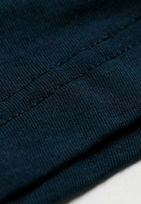 Marineblauwe stof met een ribbelstructuur, die ingewikkelde stiksels en plooien toont voor een gladde uitstraling. Zacht en flexibel materiaal.
