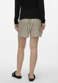 Beige stribede shorts med brune lodrette linjer, lavet af letvægtsstof. Livremmen er afslappet, og personen har sorte sandaler på.