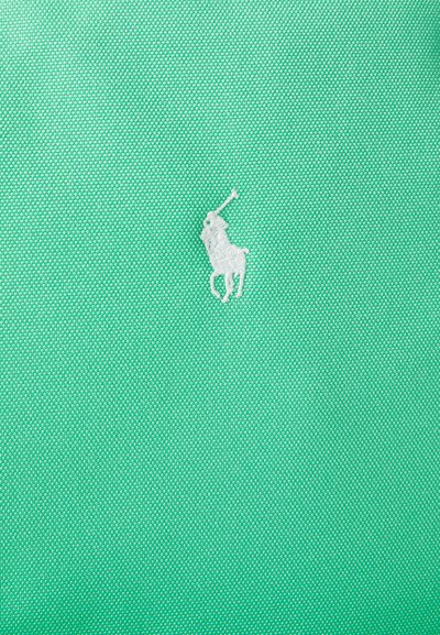 Πράσινο υφασμάτινο ύφασμα με υφή που διαθέτει ένα μικρό λευκό κεντημένο εικονίδιο ενός όρθιου πόνι με υψωμένο ραβδί.