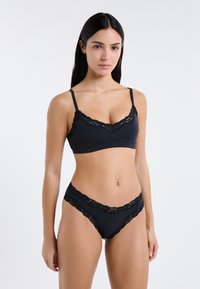 Schwarzes Bralette mit Spitzenbesatz und verstellbaren Trägern, kombiniert mit passenden High-Waist-Slips mit gewelltem Spitzenrand. Glatter, dehnbarer Stoff.