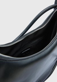 Zwarte leren tas met een gladde textuur, voorzien van een ritssluiting en een zwart stoffen interieur met een extra ritsvak.