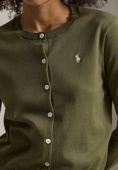 Πράσινη πλεκτή ζακέτα με στρογγυλή λαιμόκοψη, έξι κουμπιά και μικρό κεντητό λογότυπο στο αριστερό στήθος. Λεπτή υφή, casual σχεδίαση.