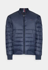 Mörkblå puffjacka med dragkedja fram, ribbade ärmmuddar och horisontell quiltning. Har en liten logga på bröstet och en kontrasterande detalj på kragen.