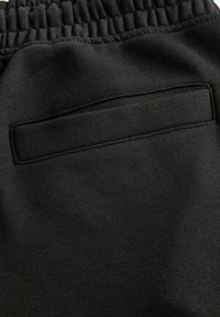 Sorte sweatpants lavet af blødt stof med en glat tekstur. Har en elastisk talje og en patchlomme på bagsiden.
