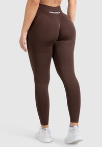 Ruskih legginsova s visokim strukom koji imaju bijeli brend logo. Tkanina izgleda glatko i tijesno prianja, naglašavajući oblik.