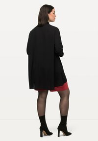 Black long-sleeve shirt with flowing back, layered over a red skirt. Black tights and ankle-high pointed heels complete the outfit.