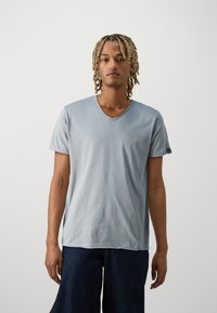 Tricou V-necă de culoare bleu deschis, fabricat dintr-un material moale; mâneci scurte cu o croială lejeră, asortat cu culotes din denim închis la culoare.