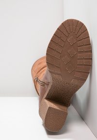 Bottine marron avec une semelle en caoutchouc texturée, un talon empilé, une fermeture éclair latérale et une tige en cuir lisse. Vue arrière mettant en évidence le motif de la semelle.